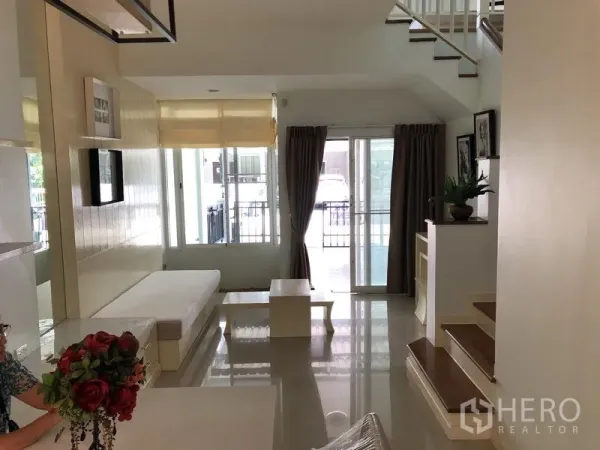 Townhouse for rent in Prawet, Bangkok - Bright living room with glossy tile floors, built-in bench, sliding glass doors and staircase.