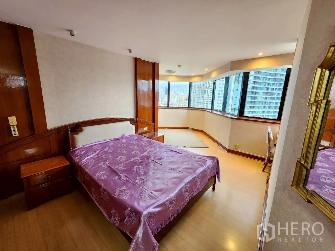 Condominium for rent in Khlong Toei, Bangkok - Master bedroom with bay windows, timber accents and Bangkok skyline view.