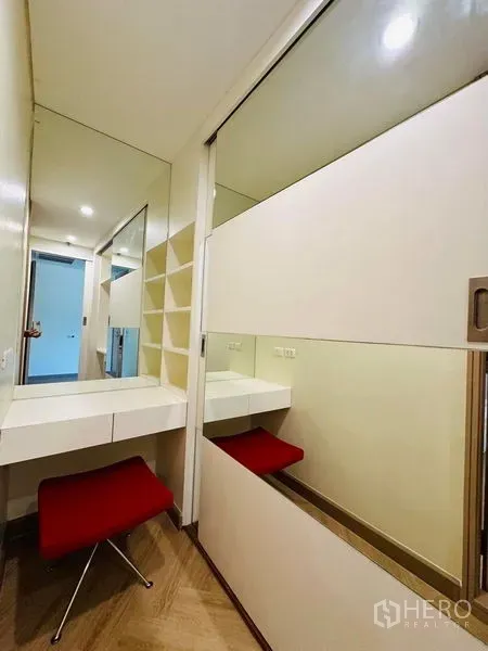 Condominium for rent in Bang Rak, Bangkok - Built-in dressing nook with mirror, shelving, and a red stool in a corridor.