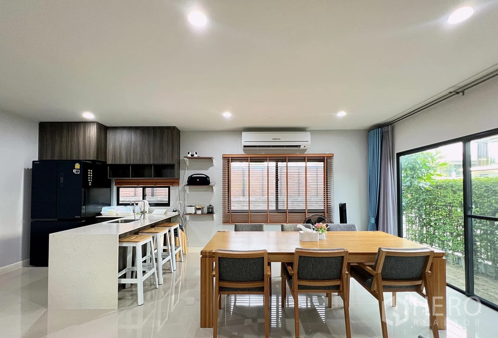 Detached House for rent or sale in Lam Luk Ka, Pathum Thani - Modern kitchen with white island breakfast bar, dark cabinets and dining table.