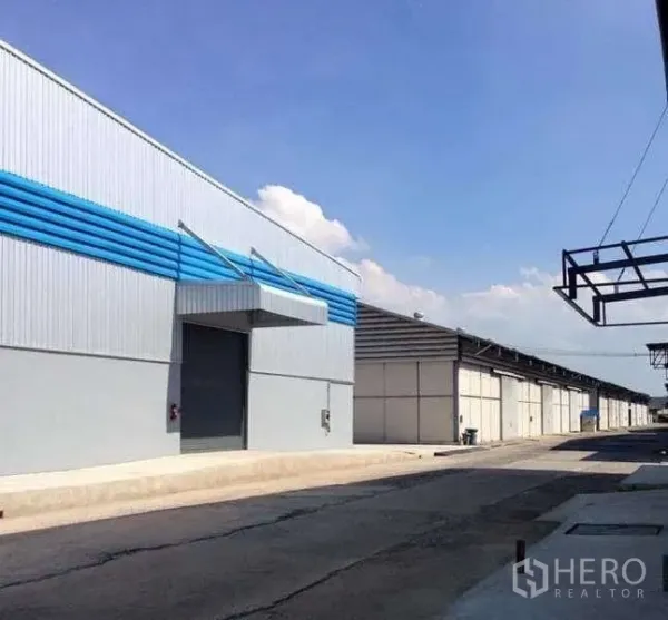 Warehouse for rent in Bang Pa-in, Phra Nakhon Si Ayutthaya - Side view of a warehouse facade with roller door and blue louver panels along a paved service road.