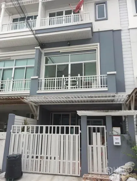Townhouse for rent in Prawet, Bangkok - Front facade of a modern multi-storey townhouse with white metal gate and balconies.