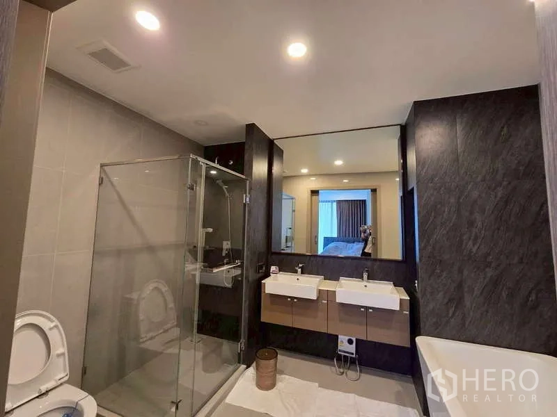 公寓 出租在Phaya Thai, Bangkok - 主卫设玻璃淋浴间、双台盆，可见浴缸一角。