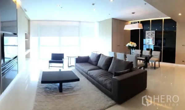 Condominium for rent in Pathum Wan, Bangkok - Bright open-plan living and dining area with floor-to-ceiling windows, large sofa and modern lighting.