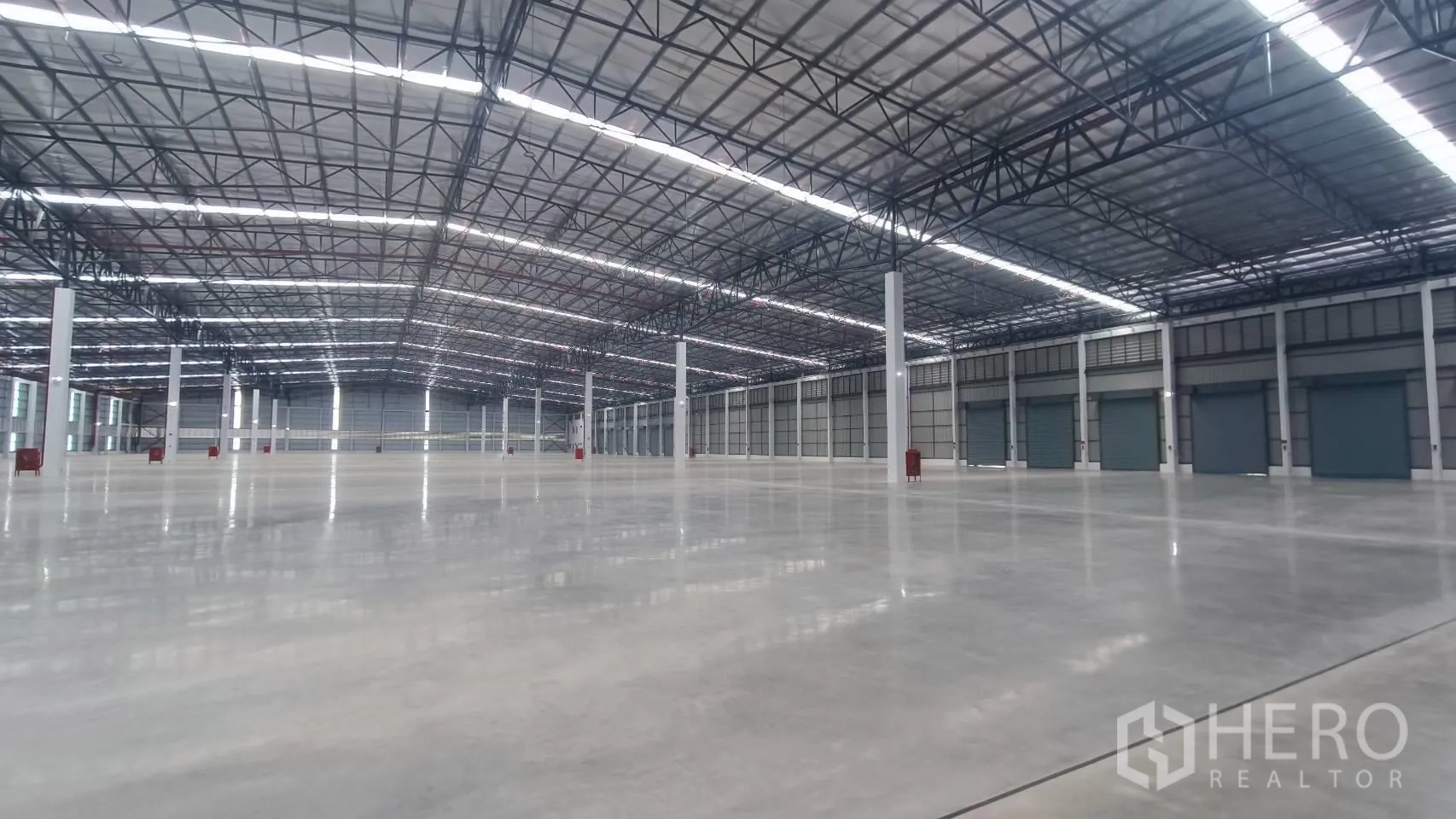 工厂 for rent in Bang Sao Thong, Samut Prakan - 大型仓库内部，抛光混凝土地面，高钢桁架屋顶与多处卷闸门。