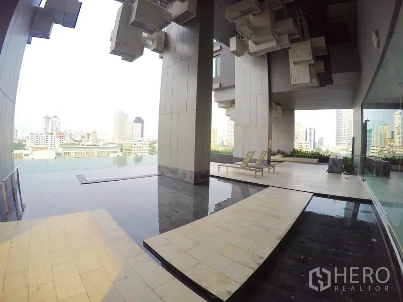 Condominium for rent in Khlong Toei, Bangkok - Condominium infinity-edge pool deck with lounge chairs and panoramic city views.