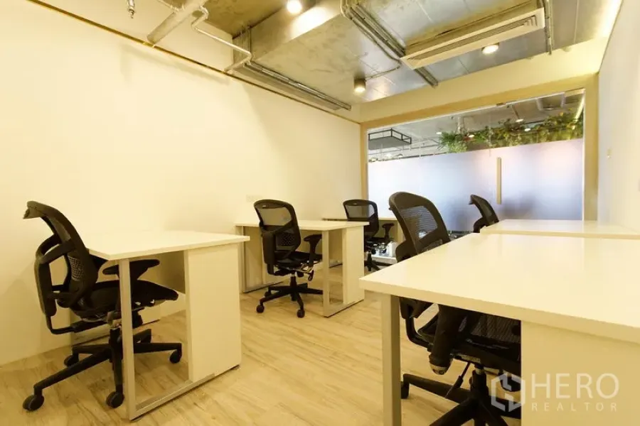 Office Space for rent in Watthana, Bangkok - Furnished private office with multiple white desks, mesh chairs, wood flooring, exposed ceiling and air-conditioning beside a frosted glass partition.
