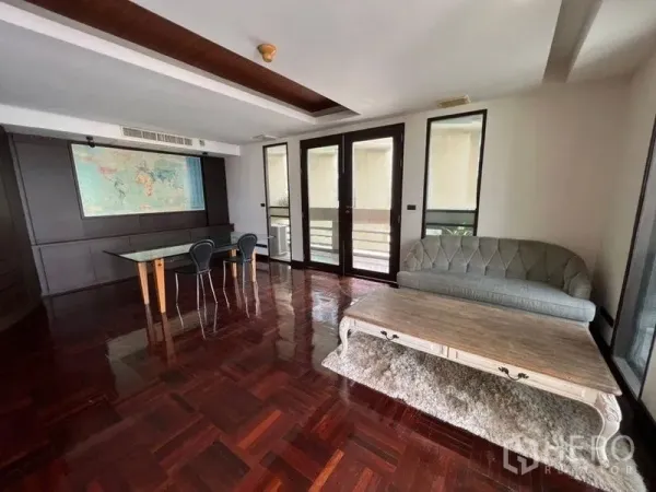 Condominium for rent in Khlong Toei, Bangkok - Multi-purpose family room with parquet floors, balcony access, sofa and glass table.