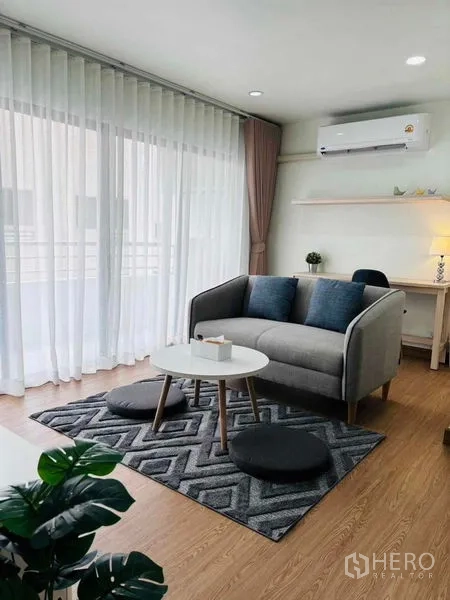 Shophouse for rent in Watthana, Bangkok - Bright living area with a gray sofa, round coffee table, sheer floor-to-ceiling curtains and balcony view.