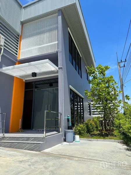 工厂 出租或出售在Lam Luk Ka, Pathum Thani - 前方办公室入口，玻璃门与金属雨棚，周边绿化。