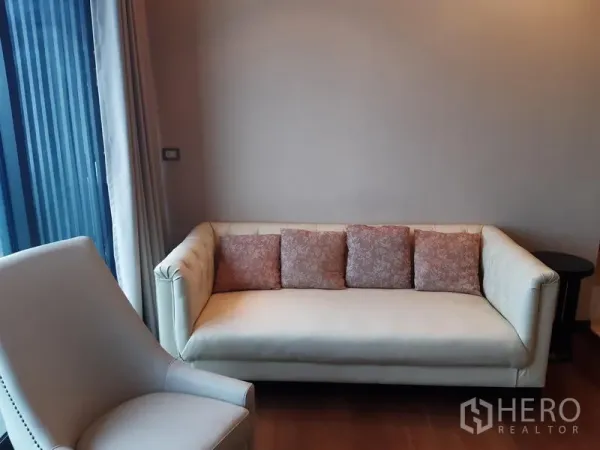 Condominium for rent or sale in Khlong Toei, Bangkok - Cozy lounge corner with cream sofa and patterned cushions beside curtain wall.