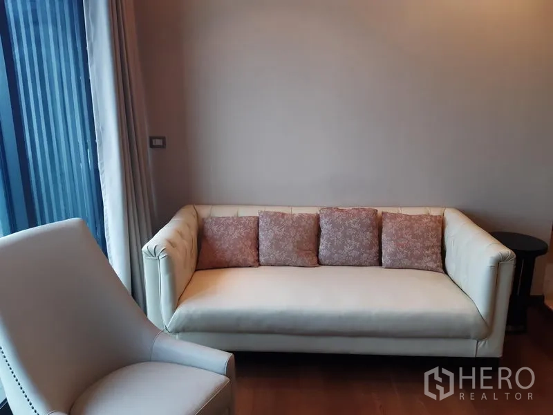 Condominium for rent or sale in Khlong Toei, Bangkok - Cozy lounge corner with cream sofa and patterned cushions beside curtain wall.