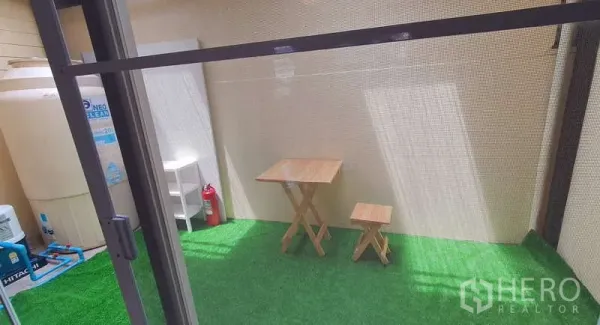 Detached House for rent in Bang Phli, Samut Prakan - Covered patio with artificial grass and a small wooden bistro set next to utility storage.
