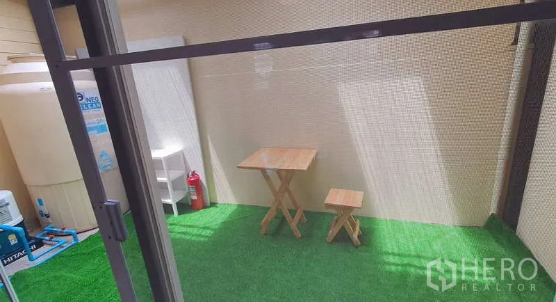 Detached House for rent in Bang Phli, Samut Prakan - Covered patio with artificial grass and a small wooden bistro set next to utility storage.