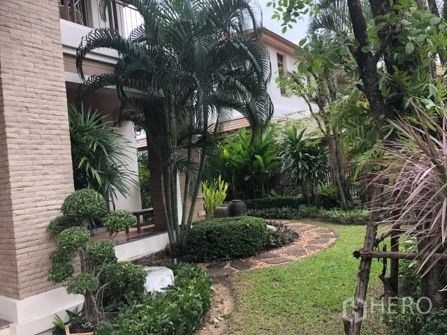 Detached House for rent in Bang Phli, Samut Prakan - Curved stone pathway through a lush side garden beside the home with palms and manicured shrubs.