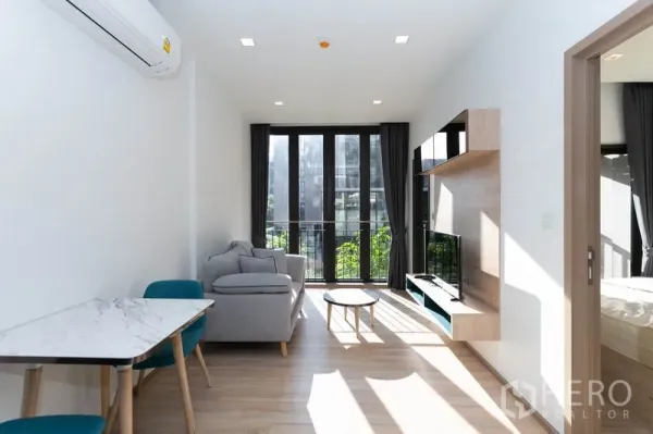 Condominium for rent in Watthana, Bangkok - Bright living room with floor-to-ceiling windows, balcony, sofa and TV unit overlooking a green courtyard.