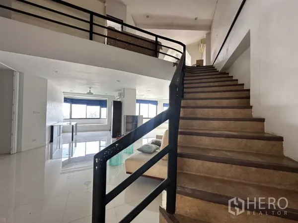 Condominium for sale in Bang Na, Bangkok - Duplex condo interior with curved staircase, glossy tiled floor and bright open-plan living area with large windows.