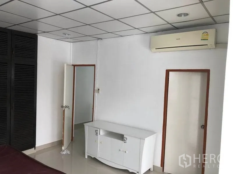 Townhouse for rent in Watthana, Bangkok - Bedroom corner with white cabinet, split-type air conditioner and two interior doors.