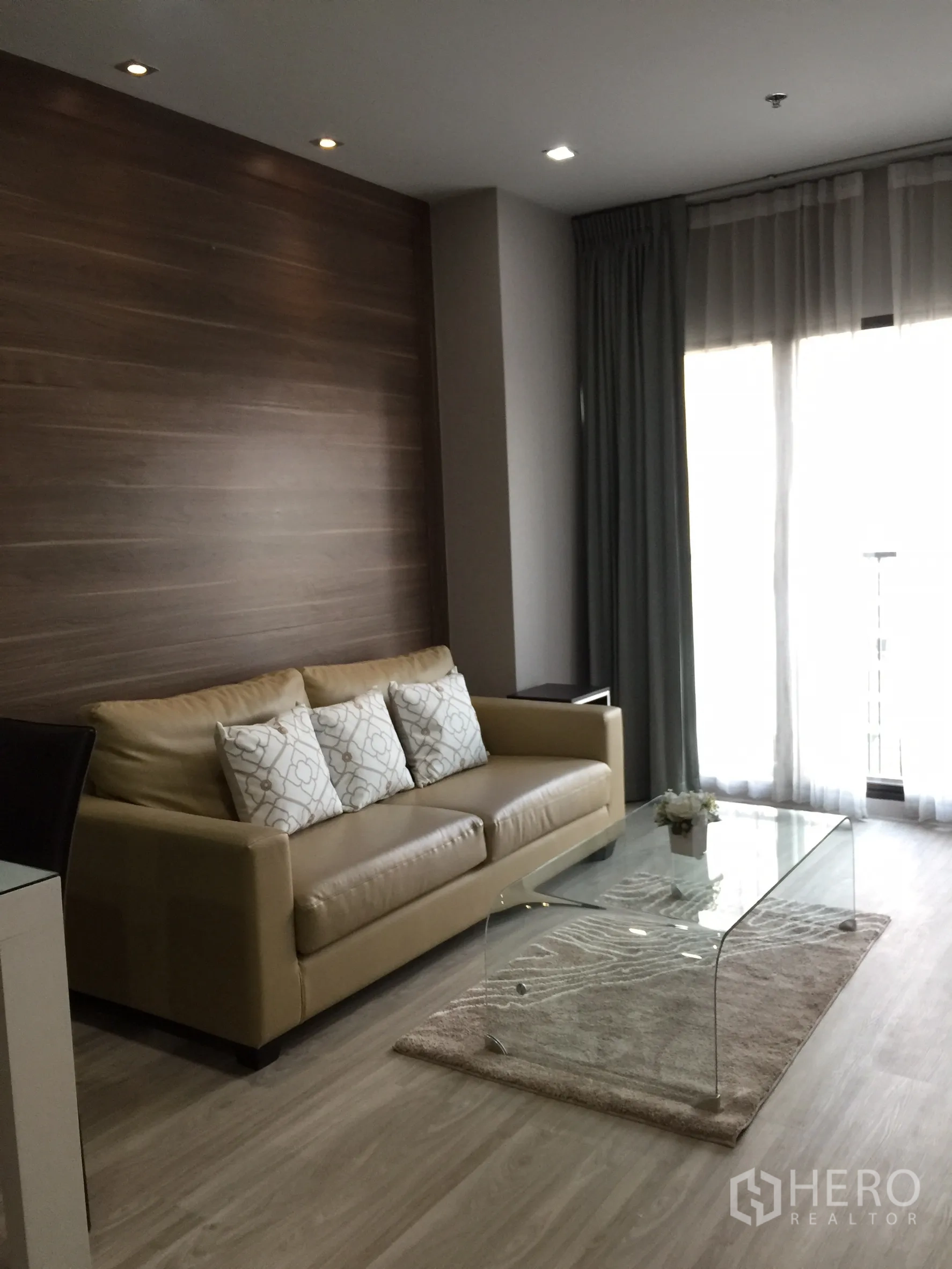 Condominium for rent or sale in Bangkok - Living area with tan leather sofa, glass coffee table and light from the balcony.