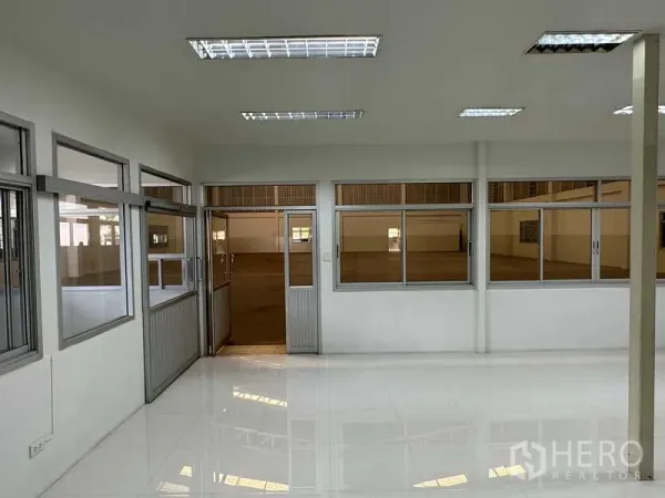 Factory for rent in Samut Prakan - Glass-partitioned office area with white tiled floors and fluorescent lighting adjoining the production hall.