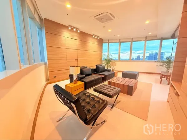 Condominium for rent or sale in Khlong Toei, Bangkok - Modern living area with spotlight ceiling, wood feature wall and black leather seating framed by wraparound windows.