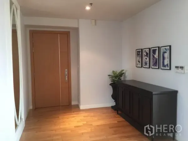 Condominium for rent in Khlong Toei, Bangkok - Bright entry hall with wooden door, dark console cabinet, framed art and light wood flooring.
