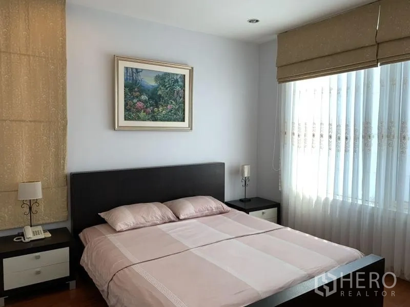 Condominium for rent in Khlong Toei, Bangkok - Airy bedroom with queen bed, large window with blinds, bedside tables, and framed artwork.