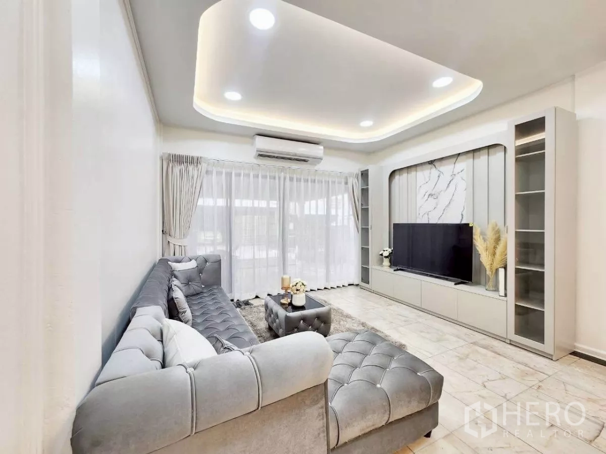 Townhouse for rent in Huai Khwang, Bangkok - L-shaped sectional facing built-in media wall with cove lighting and sheer curtains.