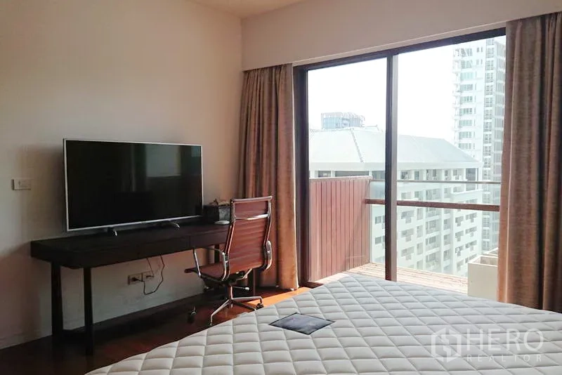 Condominium for sale in Pathum Wan, Bangkok - Bedroom with desk and TV facing a sliding glass door to a balcony with city views.
