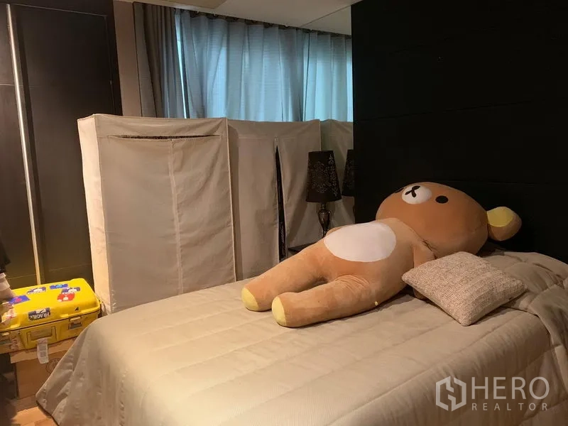 Condominium for sale in Khlong Toei, Bangkok - Cozy secondary bedroom with soft lighting, drapes and a neatly made bed.