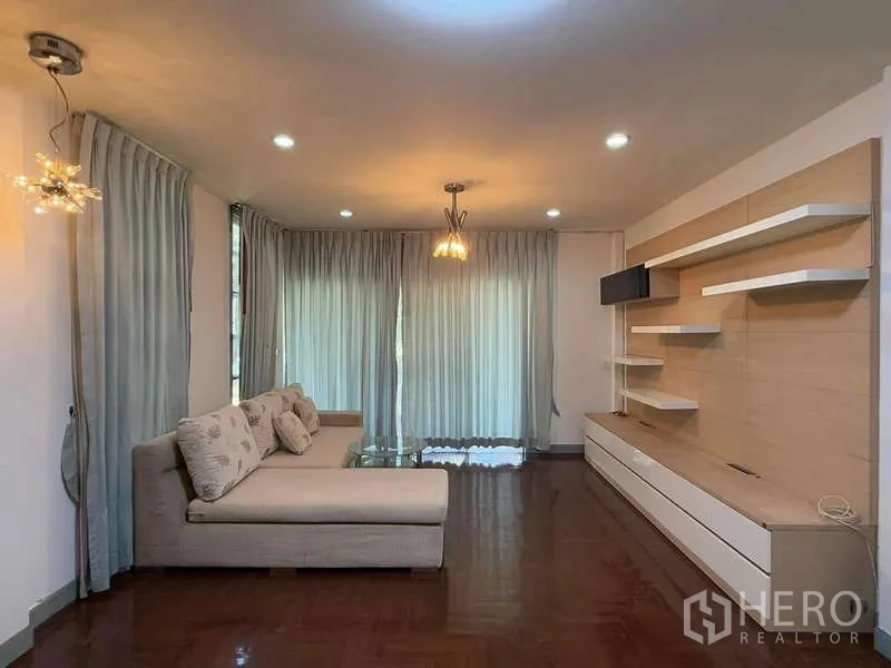 独立式住宅 出租在Bang Kapi, Bangkok - 客厅配转角沙发、墙面置物架与轻薄窗帘。