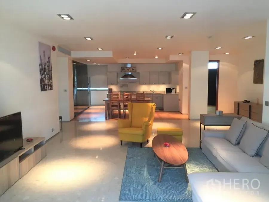 Condominium for rent in Khlong Toei, Bangkok - Open-plan living room with sofa set, yellow armchair and coffee table leading to a modern kitchen and dining area.