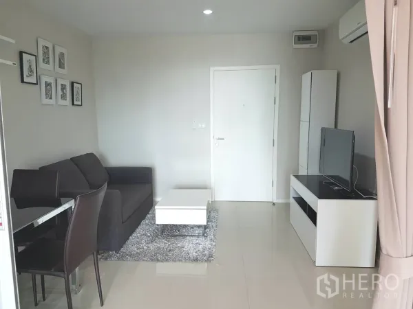 คอนโด ให้เช่าหรือขายในHuai Khwang, Bangkok - ห้องนั่งเล่นสว่างมีโซฟาสีเทา ชั้นวางทีวี และโต๊ะกลางสีขาวในคอนโดสไตล์โมเดิร์น