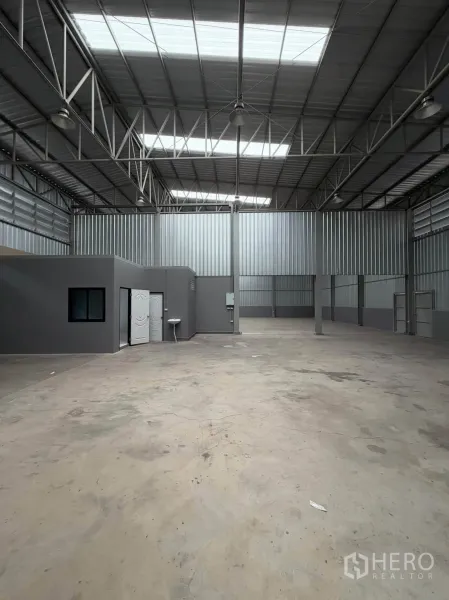 Warehouse for rent in Phra Pradaeng, Samut Prakan - Open storage area showing an internal office with window, concrete flooring, and steel-clad walls.