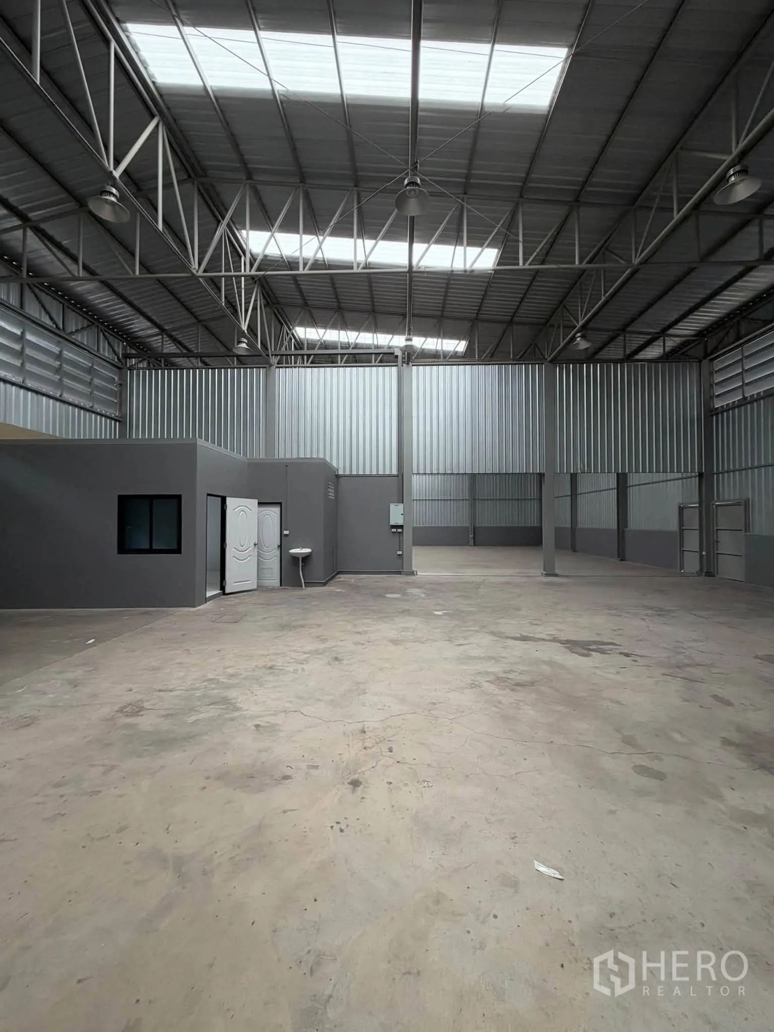 Warehouse for rent in Phra Pradaeng, Samut Prakan - Open storage area showing an internal office with window, concrete flooring, and steel-clad walls.