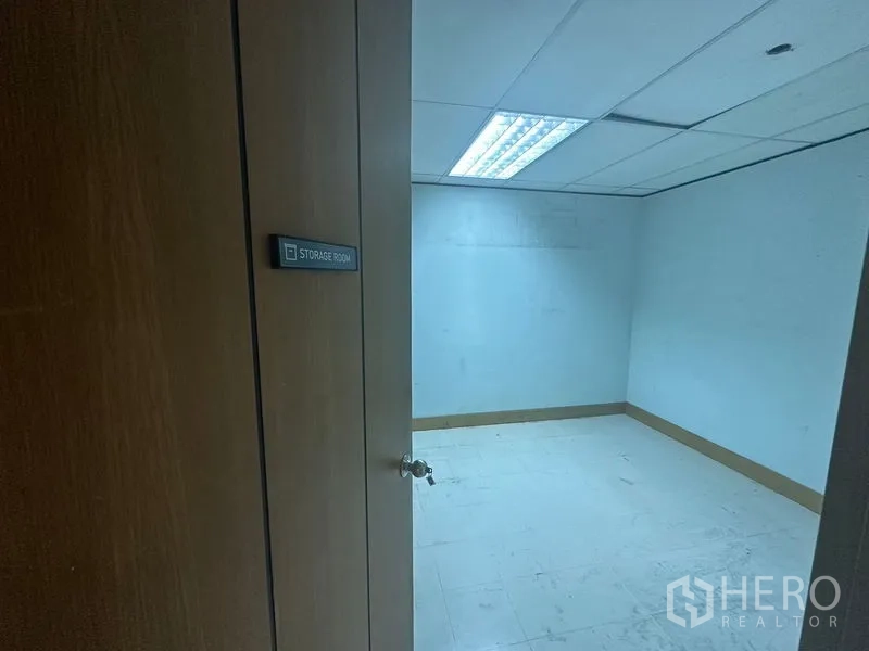 Office Space for rent in Khlong Toei, Bangkok - Compact storage room with white tile flooring and fluorescent lighting behind a wooden door.