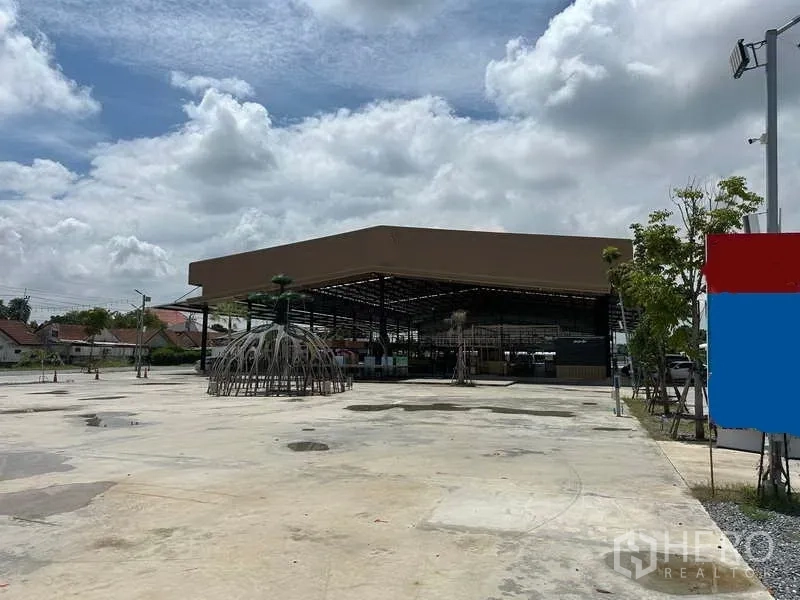 Warehouse for rent in Sai Noi, Nonthaburi - Spacious outdoor forecourt leading to a metal-roof warehouse, with low-rise homes nearby.