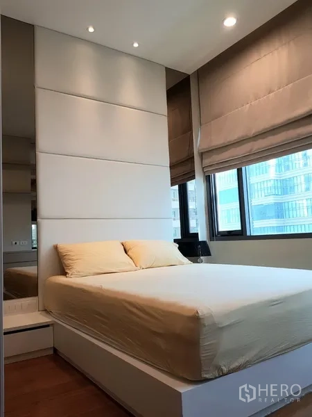 Condominium for rent in Khlong Toei, Bangkok - Cozy bedroom with upholstered headboard, double bed and corner windows with city views.