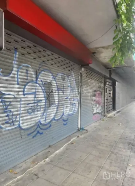 Shophouse for rent in Watthana, Bangkok - Closed metal roller shutters with graffiti along the shophouse exterior.