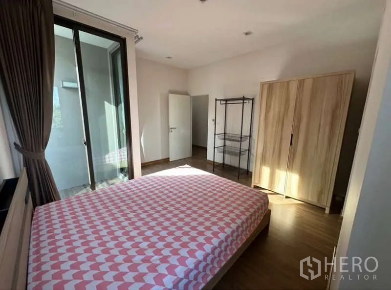 Townhouse for rent in Lat Phrao, Bangkok - Sunlit bedroom with balcony access, wood flooring and a freestanding wardrobe.