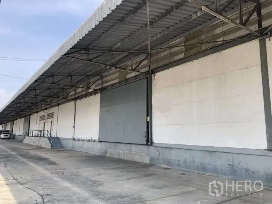 货栈 出租在Khlong Luang, Pathum Thani - 带雨棚的装卸月台一侧视角，配有坡道与台阶，沿线为卡车通道。