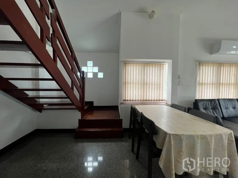 Detached House for rent in Saphan Sung, Bangkok - Dining space beside wooden staircase with table, chairs and window blinds.