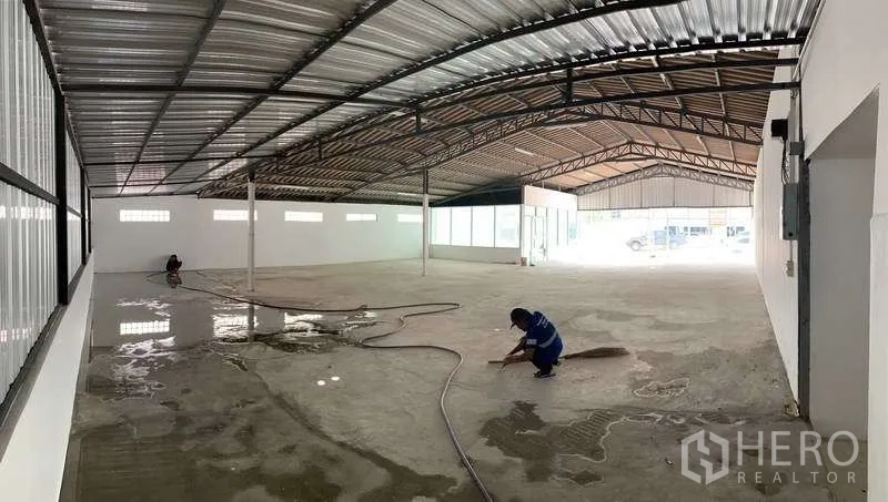 Warehouse for rent in Mueang Pathum Thani, Pathum Thani - Large warehouse bay being cleaned, wide-span metal roof, ventilation blocks and support columns.