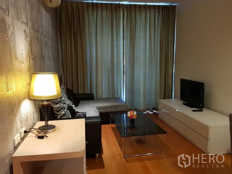 公寓 出租在Ratchathewi, Bangkok - 温馨客厅，电视柜、转角沙发、玻璃茶几与遮光窗帘。