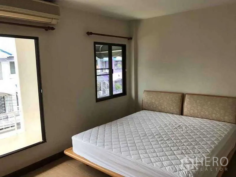 Townhouse for rent in Suan Luang, Bangkok - Corner bedroom with air conditioner, two windows and a double bed with neighborhood views.