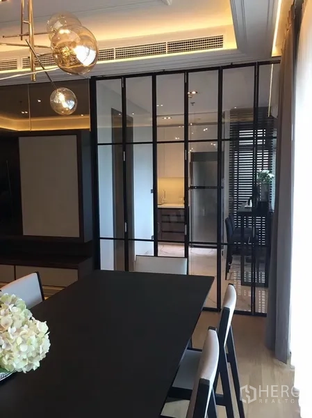 公寓 出租在Watthana, Bangkok - 餐厅配黑色餐桌椅，玻璃隔断通往厨房，吊灯点缀。
