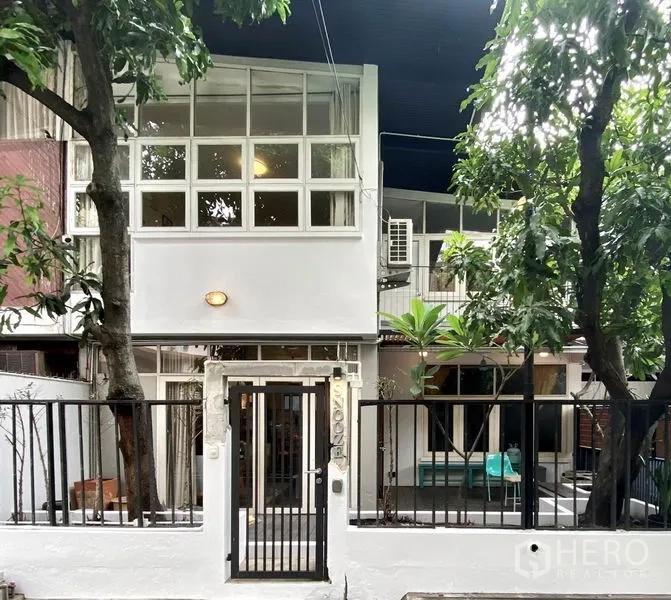 联排别墅 出租在Khlong Toei, Bangkok - 两层现代联排别墅外观，方格大窗与黑色大门，庭前有树木。