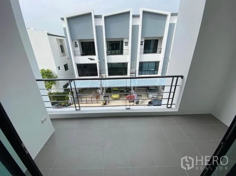 Townhouse for rent in Bang Na, Bangkok - Private balcony with tiled floor overlooking a row of modern townhouses and carports.