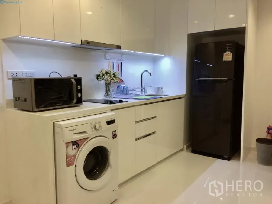 Condominium for rent or sale in Sathon, Bangkok - Modern white kitchenette featuring sink, overhead cabinets, fridge, microwave, and front-load washing machine.