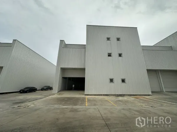 工厂 出租在Khlong Luang, Pathum Thani - 工业厂房立面，配高卷闸门与划线停车位。